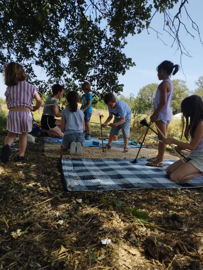 Des enfants jouent dehors avec des bâtons du diable, sur des plaids posés dans l’herbe